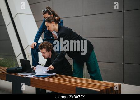 Trois jeunes professionnels collaborant à un projet tout en regardant un ordinateur portable à l’extérieur Banque D'Images