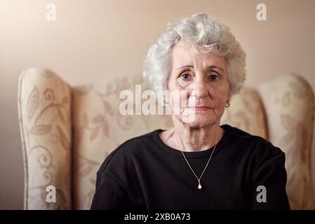 Portrait, femme âgée ou âgée à la maison pour se détendre avec bien-être ou confiance sur la chaise du salon. Appartement, dame fière ou senior reposant avec la paix Banque D'Images