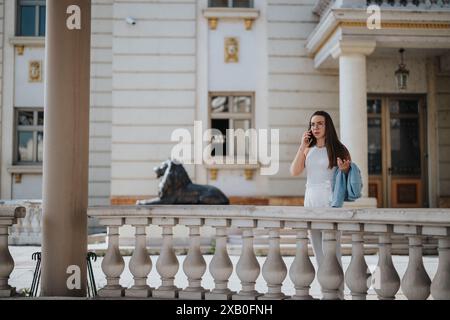 Jeune femme d'affaires parlant sur téléphone intelligent devant un bâtiment élégant à l'architecture classique Banque D'Images