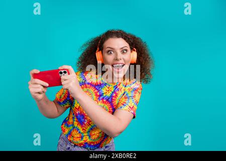 Photo d'adorable femme joyeuse porter des vêtements imprimés à la mode jouer au jeu isolé sur fond de couleur cyan Banque D'Images