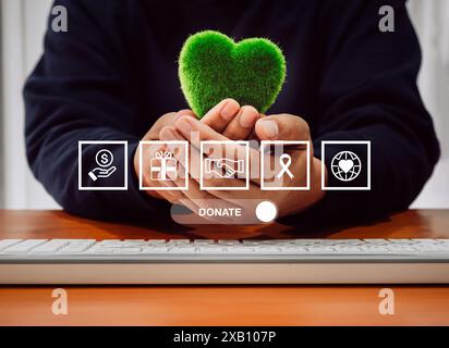 Concept de don en ligne. Le bouton de la barre de défilement « Donate » avec des icônes de charité et de collecte de fonds s'affiche sur l'écran virtuel tandis que les mains de la personne maintiennent un g vert Banque D'Images