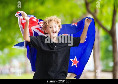 Enfant qui court avec le drapeau néo-zélandais. Petit garçon néo-zélandais acclamant l'équipe de pays. Fans de kiwi sur un terrain de sport regardant jouer en équipe. Banque D'Images