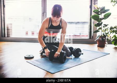 Routine d'entraînement à la maison de belle femme rousse avec haltère. Entraînement de fitness à domicile dans le salon, femme sportive portant des vêtements de sport. Banque D'Images