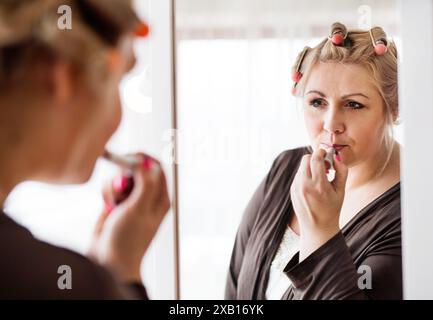 Portrait de belle jeune surpoids regardant au miroir, se maquillant le matin. Banque D'Images