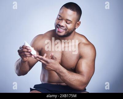 Homme noir, tube et crème en studio pour soins de la peau, pommade et cosmétiques sur fond bleu. Personne, appliquer et récipient pour dermatologie, crème solaire Banque D'Images