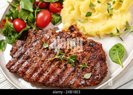 steak de porc grillé mariné dans une sauce épicée servi avec purée de pommes de terre et salade de tomates épinards fraîches sur assiette sur table en bois blanc, vue d'angle hollandais, Banque D'Images