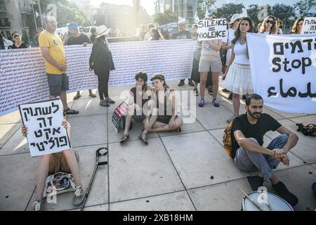 Tel Aviv, Israël. 08 juin 2024. Les manifestants israéliens sont assis par terre pendant qu'ils écoutent un discours tout en tenant des pancartes contre la guerre qui disent : «silence = violence» et «silence est un acte politique» pendant la manifestation. Des militants israéliens arabes et juifs pour la paix se sont rassemblés pour une manifestation conjointe contre la guerre Israël-Hamas à Gaza, demandant un cessez-le-feu et un accord d'otages le jour de l'opération de sauvetage des otages de Tsahal à Nuseirat. Crédit : SOPA images Limited/Alamy Live News Banque D'Images