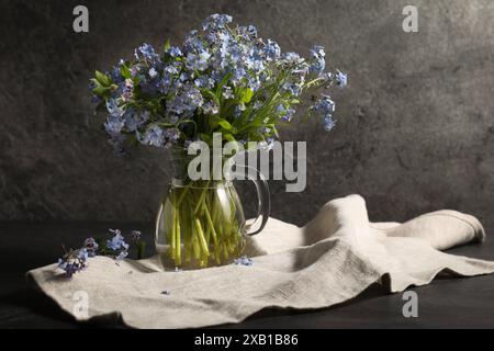 Bouquet de belles fleurs oublie-me-pas dans une cruche en verre et un tissu sur une table grise Banque D'Images