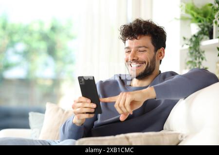 Homme heureux utilisant un téléphone intelligent assis sur un canapé dans un intérieur de maison Banque D'Images