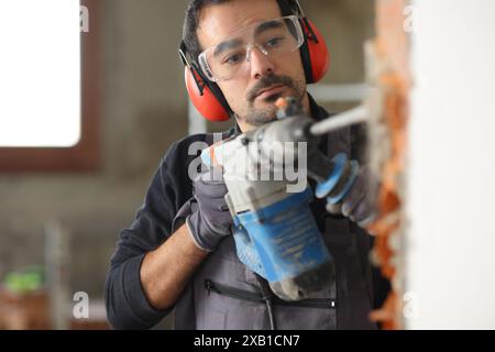 Travailleur de la construction détruit le mur à l'aide d'un marteau rotatif dans une maison en cours de réforme Banque D'Images