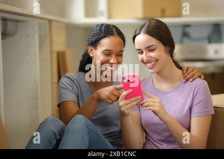 Deux colocataires heureux vérifiant le téléphone déménageant la maison dans la cuisine Banque D'Images