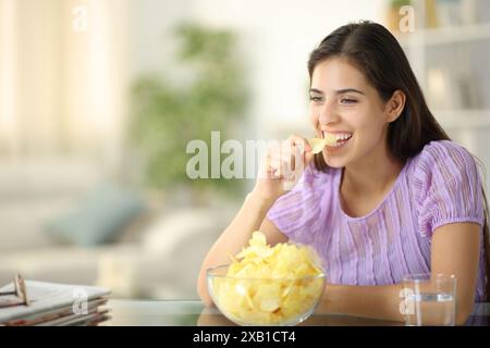 Femme heureuse riant et mangeant des chips seule à la maison Banque D'Images