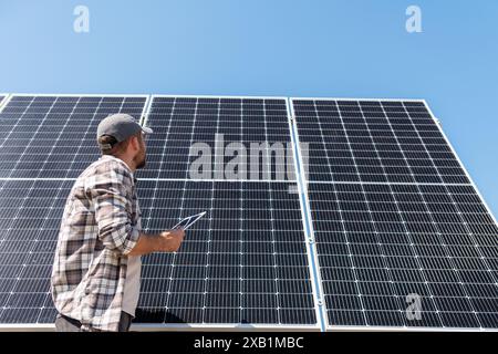 Vue à angle bas du technicien de la centrale solaire vérifie l'entretien des panneaux solaires. Foreman avec tablette numérique devant le grand panneau solaire. Banque D'Images