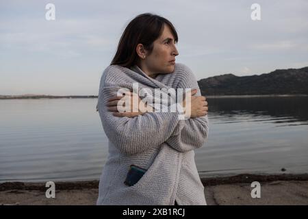 Jeune femme debout sur une plage froide et venteuse enveloppée dans une veste chaude. Banque D'Images
