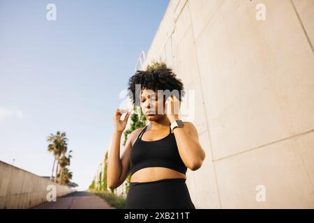 Femme ajustant ses écouteurs tout en préparant son entraînement. Jeune femme portant des vêtements de sport prêts à commencer sa routine d'exercice. Banque D'Images