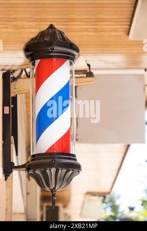 Un signe de poteau de barbier classique avec des rayures rouges, blanches et bleues à l'extérieur d'un salon de coiffure dans une zone urbaine. Banque D'Images