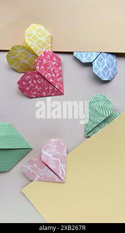 Cœurs Origami colorés dans des motifs variés disposés près des enveloppes sur fond pastel Banque D'Images