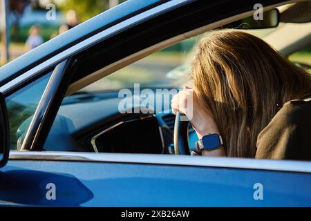 La femme est assise à l'intérieur de la voiture avec sa tête reposant sur le volant. La conductrice a des problèmes avec la conduite. Personne déprimée avec des signes d'émotion Banque D'Images