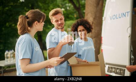 Joyeuse équipe de jeunes volontaires préparant des rations d’aide humanitaire, de la nourriture, des dons et chargeant des boîtes de carton dans une fourgonnette un jour ensoleillé. Les travailleurs caritatifs travaillent dans le Centre de dons humanitaires. Banque D'Images