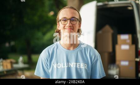 Portrait d'un jeune volontaire masculin attrayant. Joyeux homme caucasien en lunettes, portant un T-shirt bleu, souriant, posant pour caméra. Aide humanitaire, Centre de dons et concept de volontariat. Banque D'Images