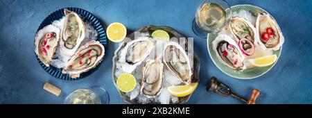 Panorama d'huîtres sur glace, avec diverses garnitures et vin blanc, plan de pose à plat au-dessus sur un fond d'ardoise bleu Banque D'Images