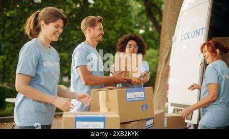 Joyeuse équipe de jeunes volontaires préparant des rations d’aide humanitaire, de la nourriture, des dons et chargeant des boîtes de carton dans une fourgonnette un jour ensoleillé. Les travailleurs caritatifs travaillent dans le Centre de dons humanitaires. Banque D'Images