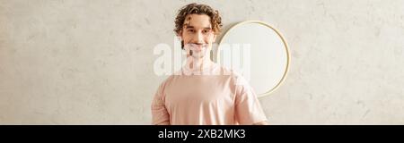Un bel homme dans des vêtements de maison confortables se tient devant un miroir rond. Banque D'Images