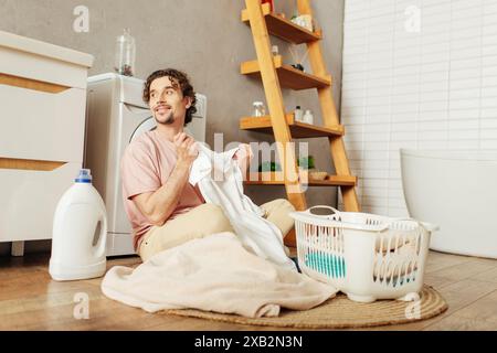 Bel homme dans les vêtements de maison assis sur le sol triant le linge. Banque D'Images