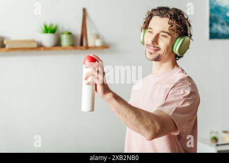 Jeune homme dans les écouteurs tient le flacon pulvérisateur pendant le nettoyage. Banque D'Images