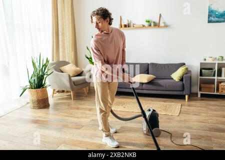 Un bel homme dans des vêtements confortables utilise un aspirateur pour nettoyer son salon. Banque D'Images