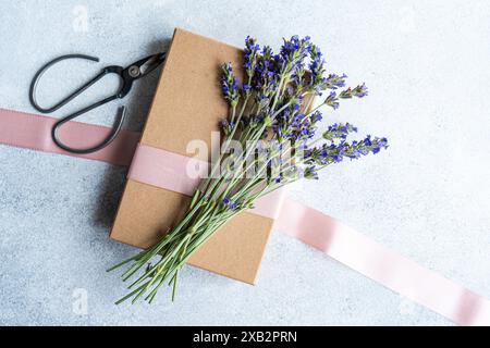 Concept de table d'été élégant mis en valeur par des fleurs de lavande fraîches, soigneusement présenté à côté d'une boîte cadeau enveloppée dans du papier brun et un ribbo rose Banque D'Images