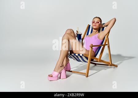Femme élégante aux cheveux blonds se détend dans une chaise de plage portant des talons hauts roses. Banque D'Images