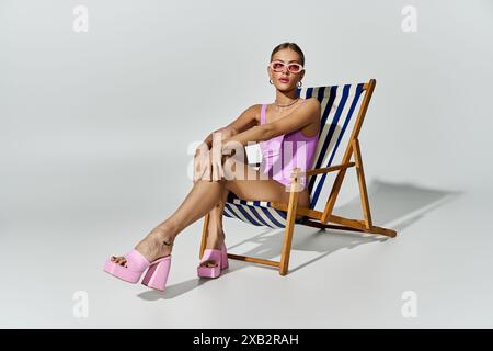 Femme blonde en maillot de bain chic se détend en chaise longue portant des talons roses. Banque D'Images