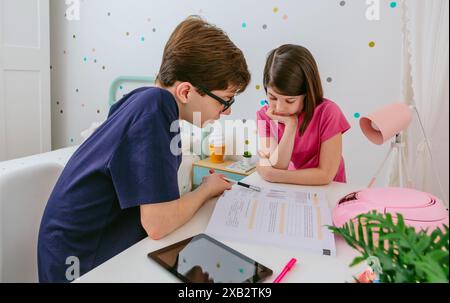 Un jeune garçon et une fille se concentrant sur les devoirs à un bureau blanc dans une chambre avec un mur en pointillés ludique Banque D'Images