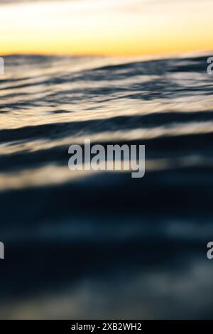 Gros plan des vagues douces de l'océan avec une mise au point douce, sous un ciel de coucher de soleil serein. Banque D'Images