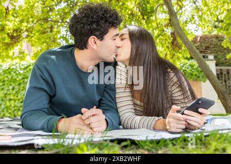 Un jeune couple profite d'un moment romantique, partageant un baiser tout en se prélassant sur une couverture dans un jardin luxuriant l'homme embrasse sa partenaire affectueusement comme elle Banque D'Images