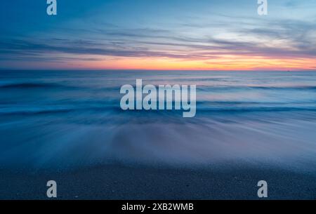 Un coucher de soleil tranquille peint l'horizon avec des teintes chaudes au-dessus des vagues douces à Atlanterra Beach en Espagne. Banque D'Images