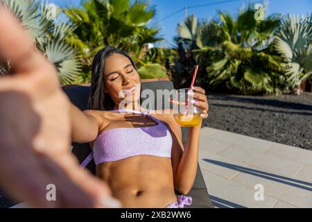 Une femme latine aime une journée ensoleillée se prélasser avec un verre, les yeux fermés et un sourire détendu. Banque D'Images