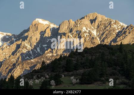 La lumière chaude du soleil baigne les montagnes enneigées de la Valle de Liebana, créant un contraste saisissant avec la forêt sombre en contrebas. Banque D'Images