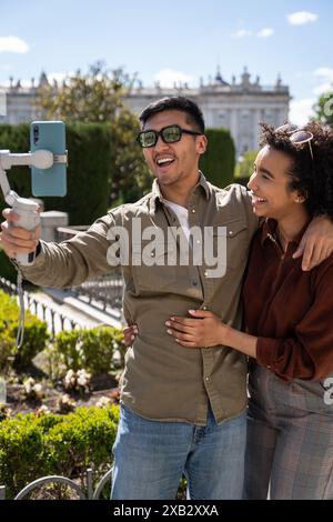 Un joyeux couple multiethnique, un Chinois et une femme hispanique, posent pour un selfie dans un jardin ensoleillé de Madrid, en Espagne. Ils sourient chaleureusement, incarnant Banque D'Images