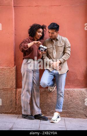 Un couple diversifié, un Chinois et une femme hispanique, examinent un appareil photo vintage appuyé contre un mur rouge à Madrid, en Espagne. Ils apprécient th Banque D'Images