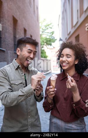 Un joyeux couple multiethnique, un homme chinois et une femme hispanique, dégustez de la crème glacée ensemble dans une charmante rue de Madrid, en Espagne, créant chaud et h. Banque D'Images