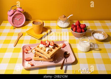 Une scène de petit-déjeuner vivante avec une gaufre garnie de fraises et de crème fouettée, présentée avec une tasse de café, un bol de fraises, et ing Banque D'Images