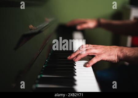 Un cliché intime capture les mains d'une personne jouant doucement un vieux piano usé, en mettant l'accent sur le mouvement et les touches poussiéreuses Banque D'Images