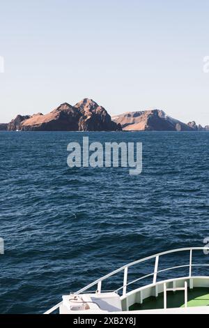 Vue depuis un bateau montrant l'étendue sereine de l'océan menant aux falaises escarpées des îles Westman, sous un ciel dégagé Banque D'Images