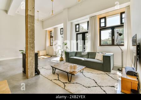 Un intérieur spacieux et moderne de salon bénéficiant de hauts plafonds, de grandes fenêtres avec rideaux, un canapé confortable et un décor minimaliste. Banque D'Images