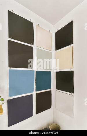 Des échantillons de différentes couleurs accrochés sur des clips contre un mur d'angle blanc pour la planification de la décoration intérieure. Banque D'Images
