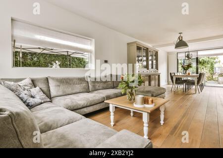 Salon spacieux et élégant avec un grand canapé gris, table à manger en bois et vue sur le jardin par de larges portes coulissantes dans une maison d'Amsterdam lo Banque D'Images