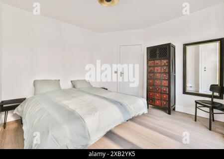 Cette chambre calme et minimaliste dispose de lits jumeaux avec literie claire, d''une armoire noire ancienne avec tiroirs rouges, d''un grand miroir mural et d''un parquet Banque D'Images