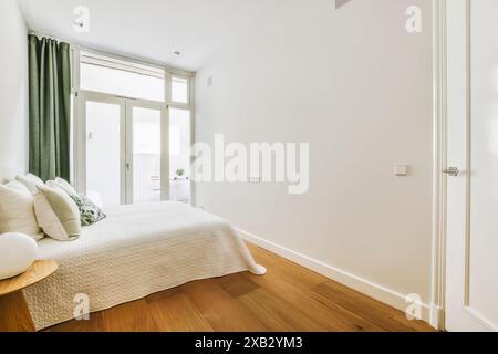 Une chambre lumineuse et confortable avec un lit confortable avec des draps blancs, de grandes fenêtres permettant la lumière naturelle, et un décor simple et minimaliste. La chambre Banque D'Images